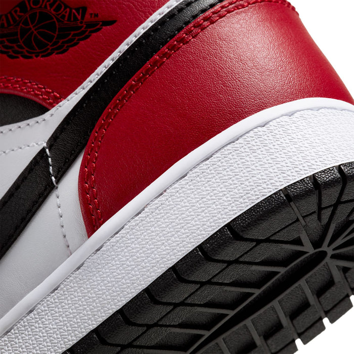 Close-up of youth sneaker side and outsole edge with red leather, black trim, and white midsole