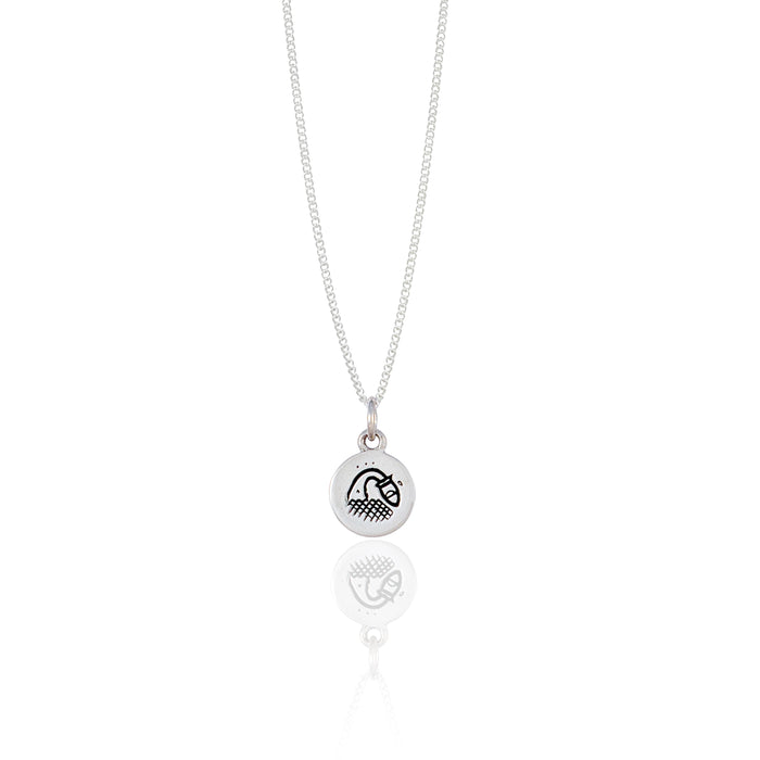 A small round silver necklace adorned with a minimalistic geometric design reflected on a white surface