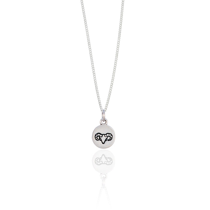 A small round silver pendant adorned with a minimalistic geometric design reflected on a white surface.