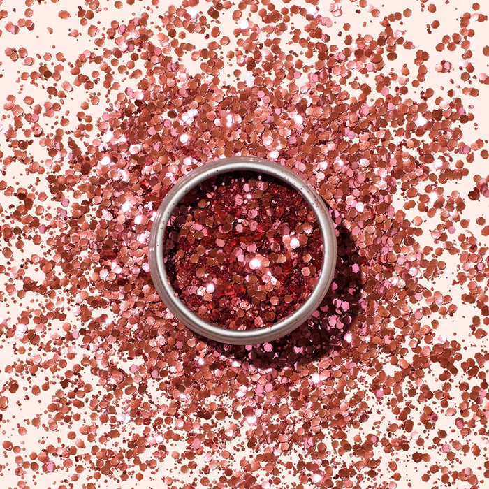 Manucurist’s Biodegradable Glitter, presented in a round metal container, shines in pink hues—ideal for nail art—while pink glitter is scattered across a light beige surface.