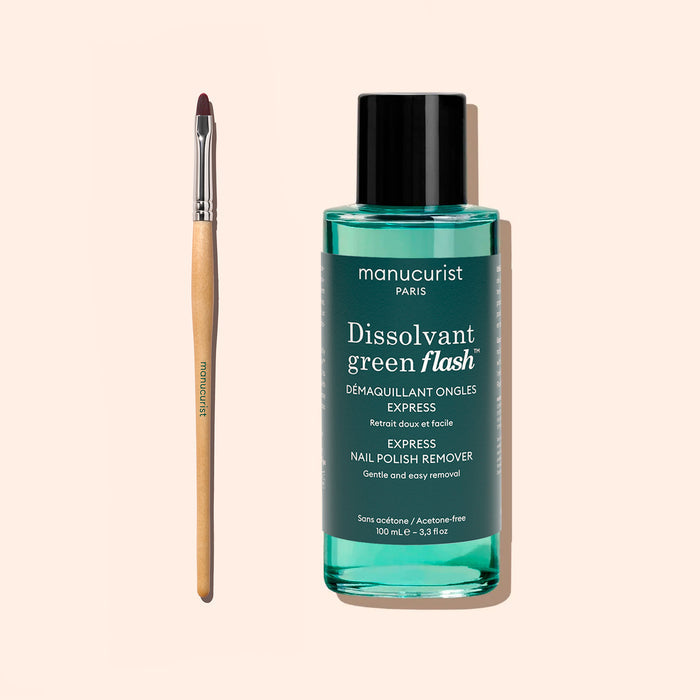 A bottle of Manucurist Green Flash nail polish remover stands next to the Manucurist Flat Brush, a thin brush with a pointed, wooden handle—both arranged on a light beige background and ideal for precise manicure and cuticle care.