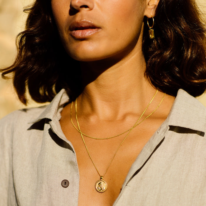 Close-up of a woman wearing gold necklaces and earrings with a blurred background