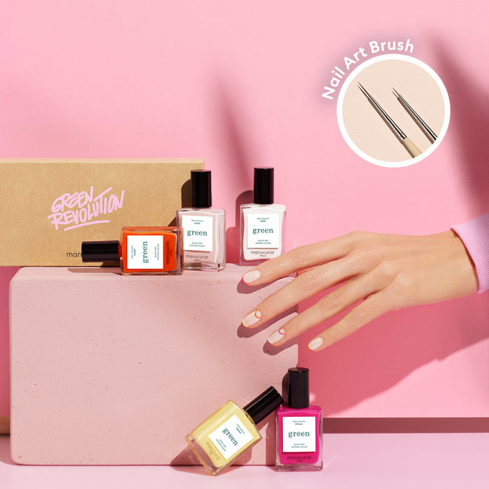A hand with pastel summer nail art from the Smile! collection by Manucurist holds a pink block, surrounded by four Green Revolution nail polish bottles and a box; a circular inset shows the Nail Art Brush up close on a pink background.