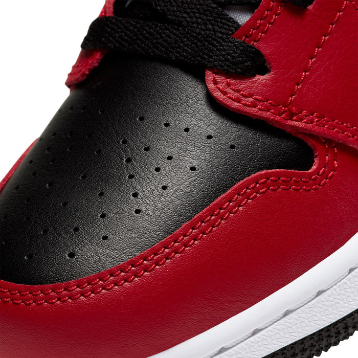 Close-up of youth sneaker toe and side panels in black with red overlays and perforations