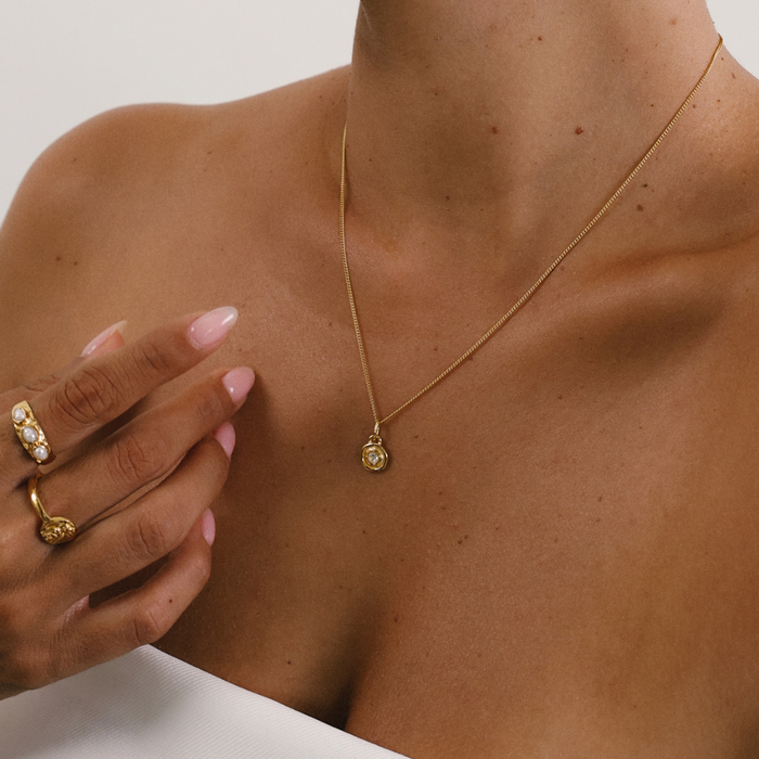 Gold necklace with a pendant worn by a person, with a hand touching the neck.