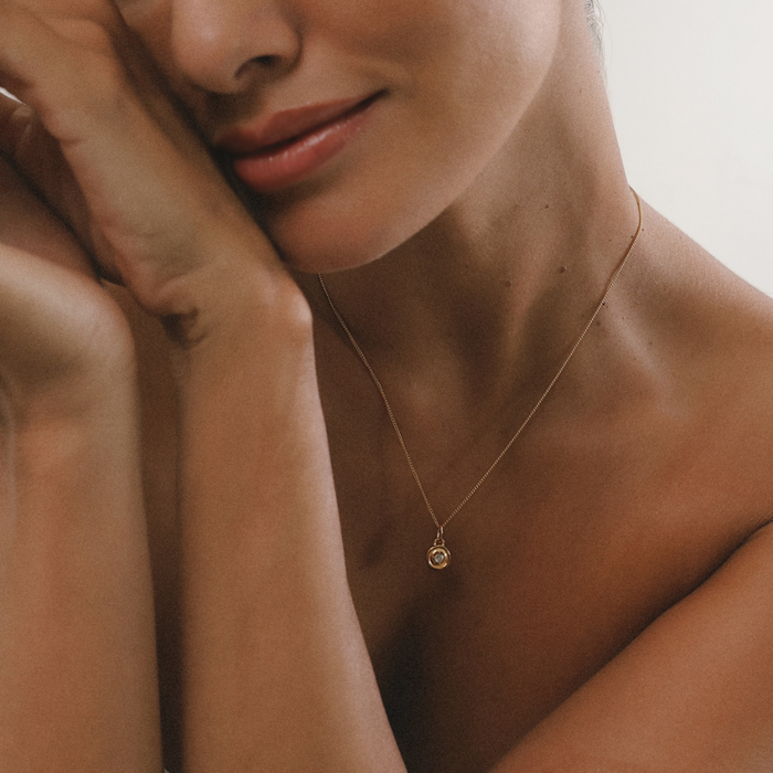 Close-up of a woman wearing a delicate gold necklace with a small pendant.