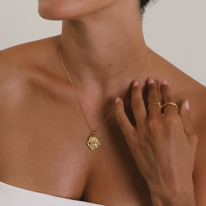 Gold necklace with a pendant worn by a person, with a hand touching the neck.