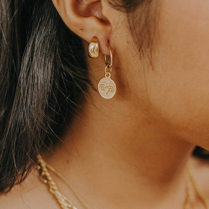 A close up of a woman wearing small round gold earrings with a minimalistic geometric design