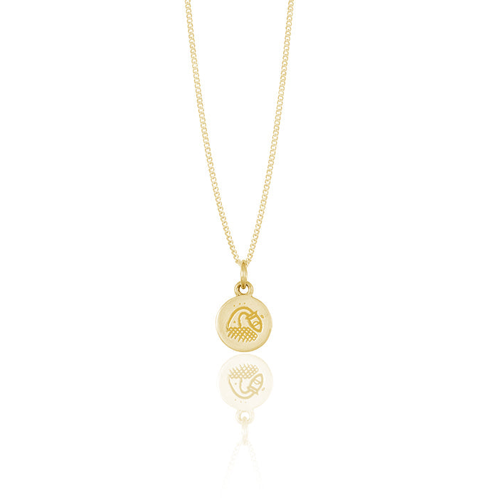 A small round gold pendant adorned with a minimalistic geometric design reflected on a white surface.