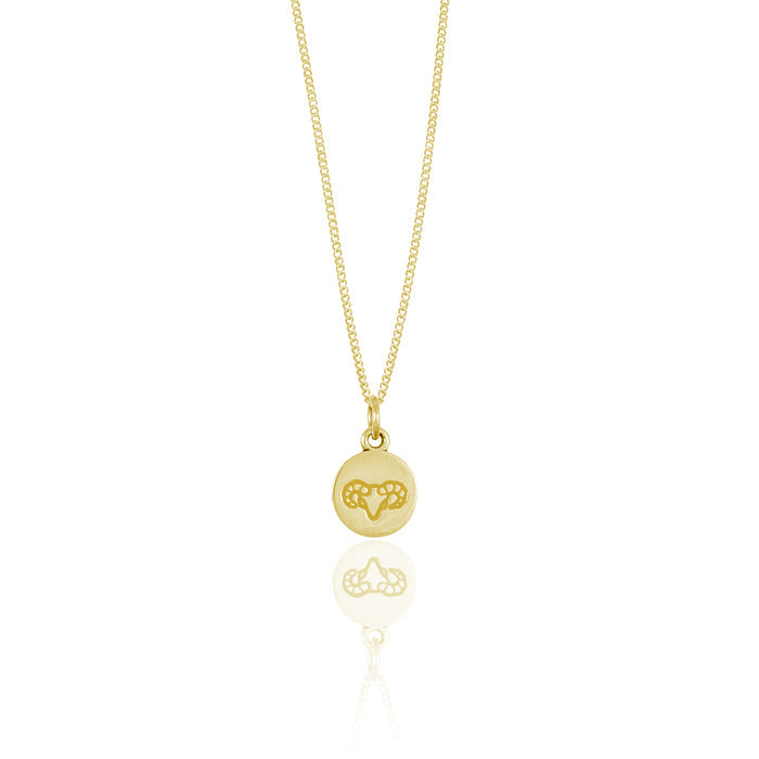 A small round gold pendant adorned with a minimalistic geometric design reflected on a white surface.