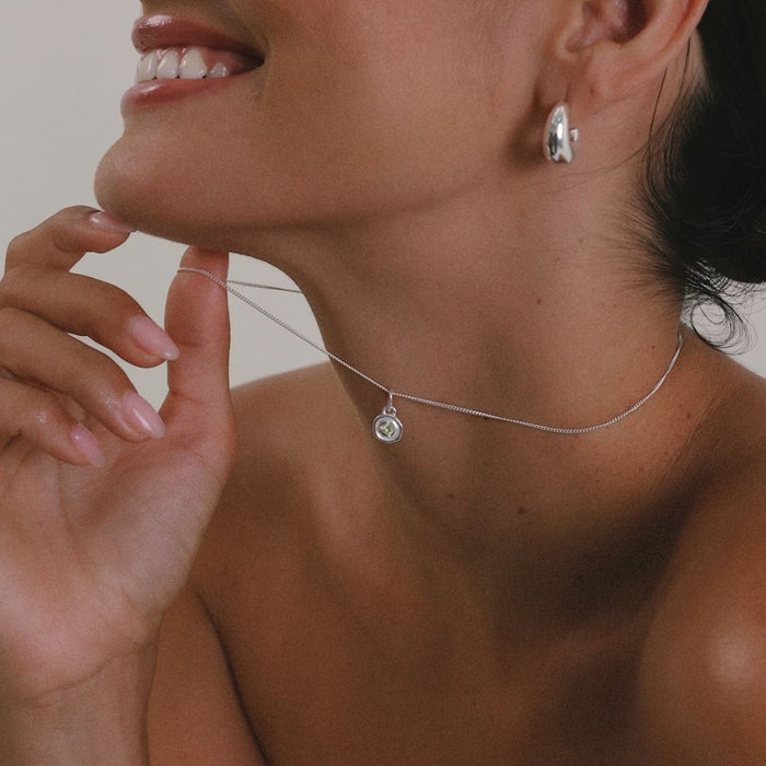 A woman wearing a sterling silver necklace featuring a vibrant green peridot birthstone charm