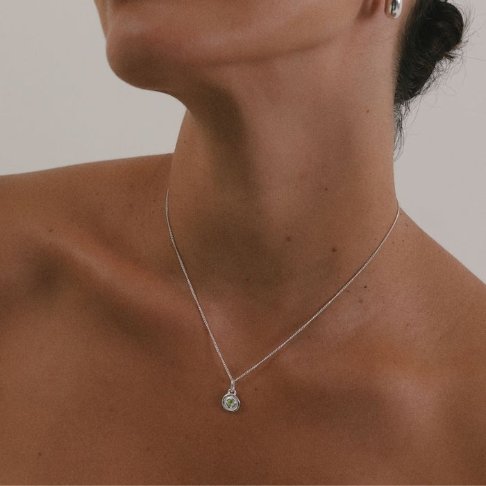 Close-up of a person wearing a silver necklace with a pendant against a neutral background