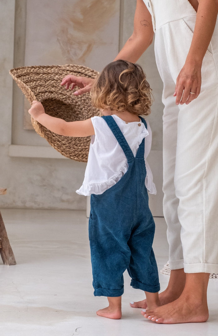 A toddler in blue overalls and a white shirt holding a hat
