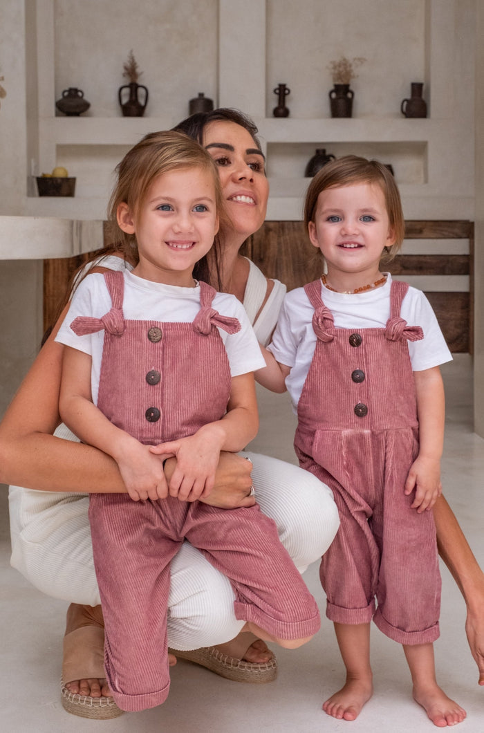 A woman posing together with two childern in their pink overalls