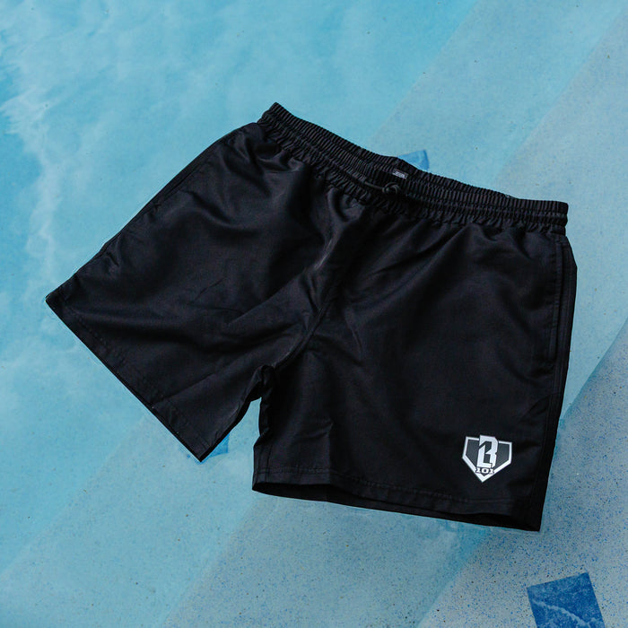 BL101 black swim trunks laid on a light blue pool surface with the gray home plate logo on the leg.