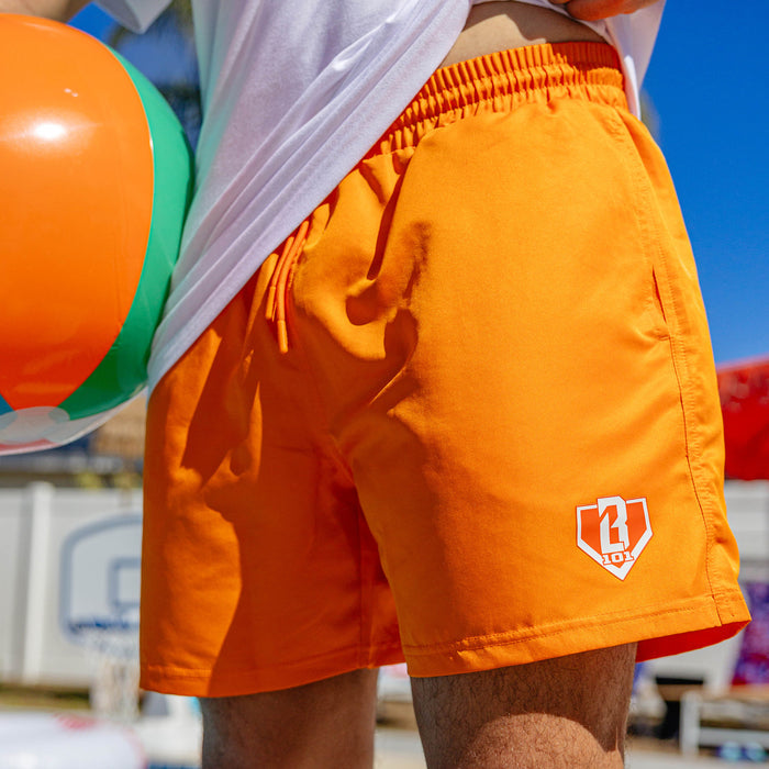 Close-up of orange BL101 swim trunks with white BL101 home plate logo on the front left leg.