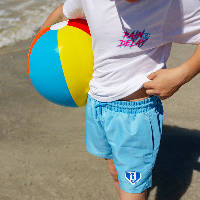 Youth model holding a beach ball showing the elastic drawstring waistband and BL101 logo on light blue youth swim trunks.