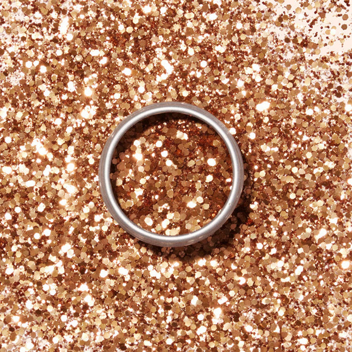 A silver ring rests on a surface dusted with Manucurist Biodegradable Glitter, creating a festive and elegant backdrop.