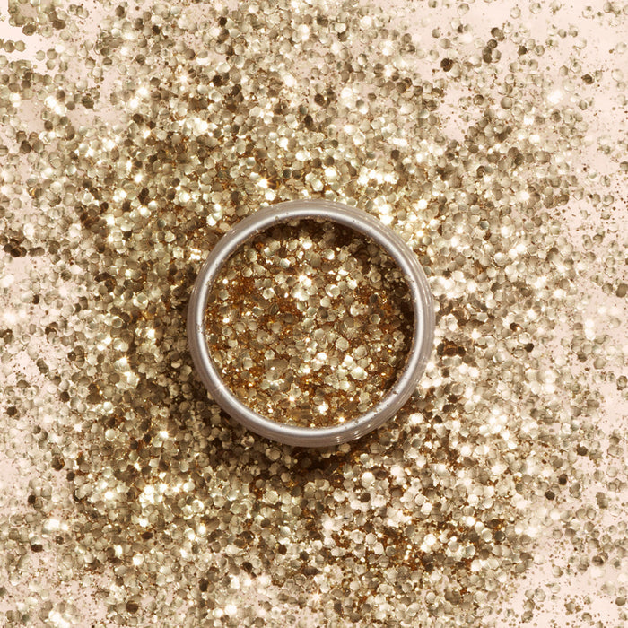 A silver ring rests on a surface sprinkled with Manucurist Biodegradable Glitter, with more plant cellulose-based glitter by Manucurist filling the inside of the ring.