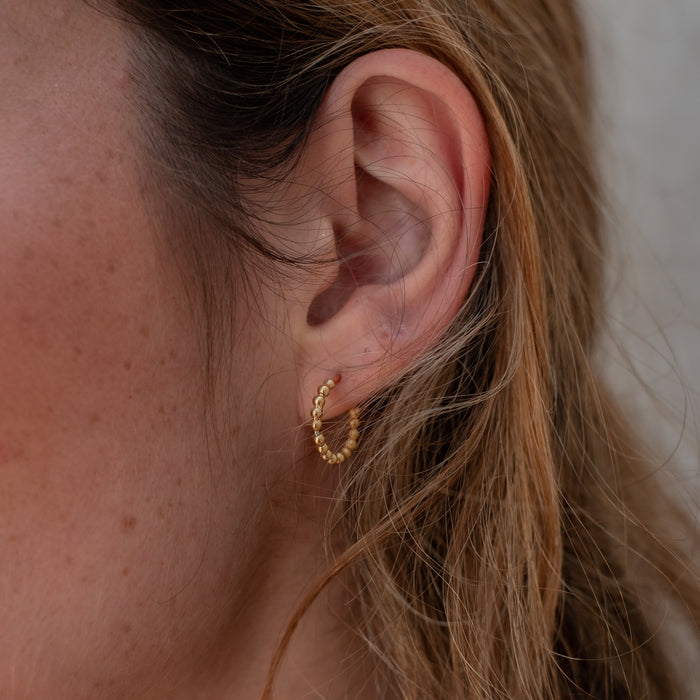 A woman with brown hair wearing a thin gold beaded earring