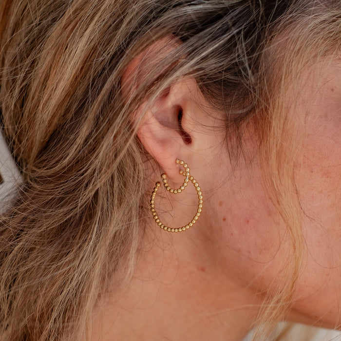 Close-up of a woman with brown hair wearing two gold earrings in different sizes