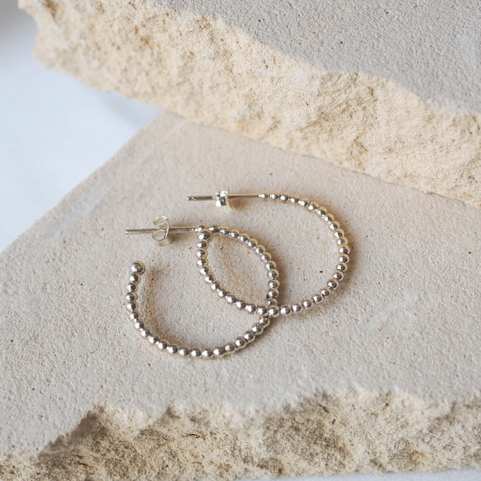 Silver beaded earrings displayed on a textured beige stone