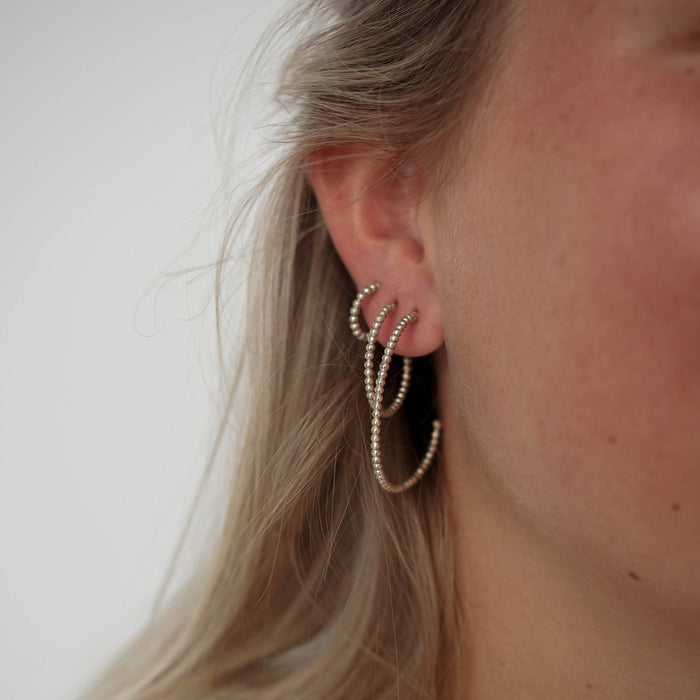 A woman with blonde hair wearing multiple silver earrings in different sizes