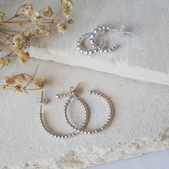 Multiple silver earrings displayed on a textured beige stone