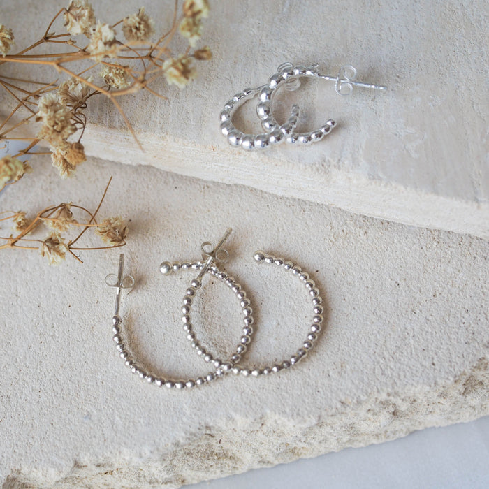 Multiple silver earrings displayed on a textured beige stone