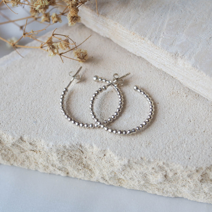 Silver beaded earrings displayed on a textured beige stone