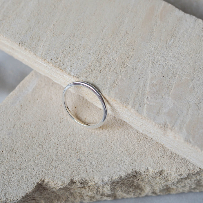 A single silver ring displayed on a textured beige stone, against a soft white background.