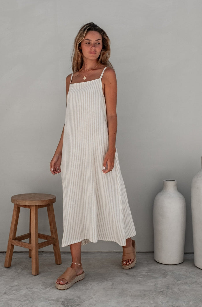 A woman with blonde hair in a striped dress, looking down placed in a minimalistic indoor setting.