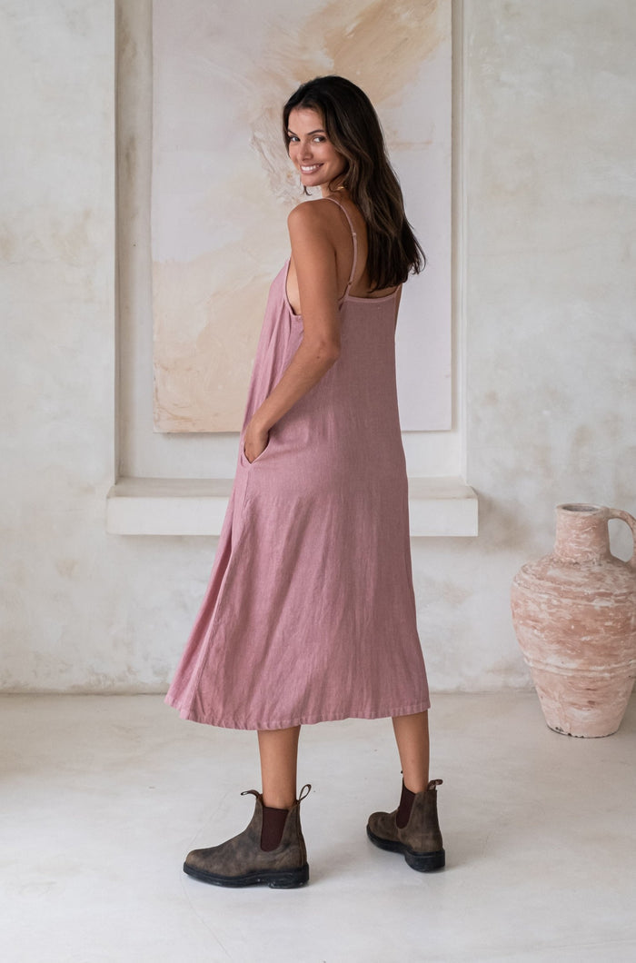 A woman wearing a pink midi dress and green boots while looking over her shoulder in a minimalistic outdoor setting.