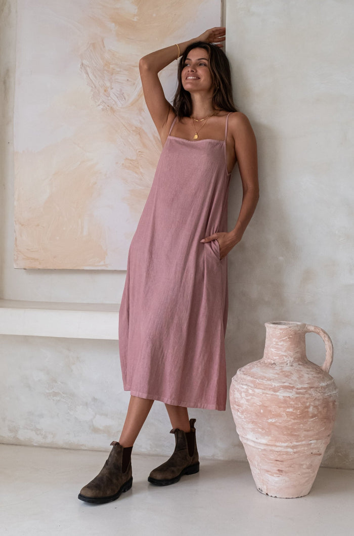 A woman laying back to a wall while wearing a pink midi dress and green boots