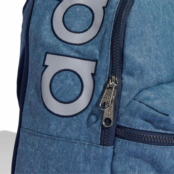 Light denim backpack front with stitched two-tone logo patch and silver zipper pull