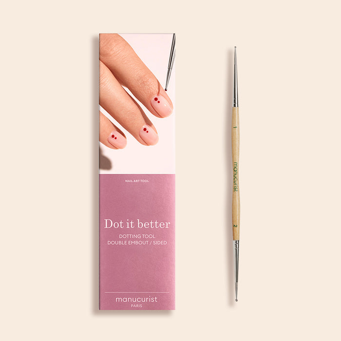 The Manucurist Dotting Tool, a double-ended nail art tool with an FSC wood handle, is displayed beside its pink “Dot it better” package featuring a hand with pale pink nails dotted in red.