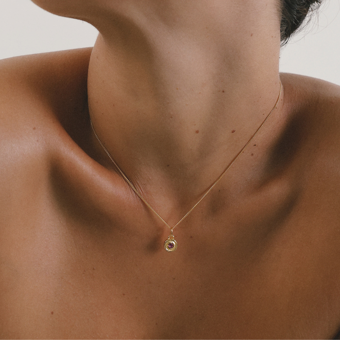 Gold necklace with a pendant on a person's neck against a neutral background