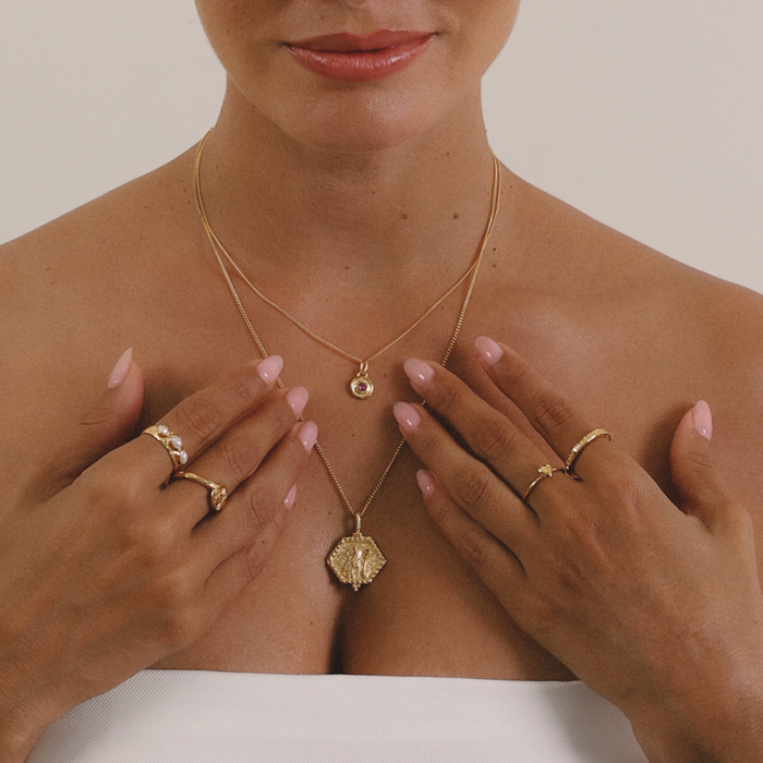 Woman wearing gold necklaces and rings on a neutral background