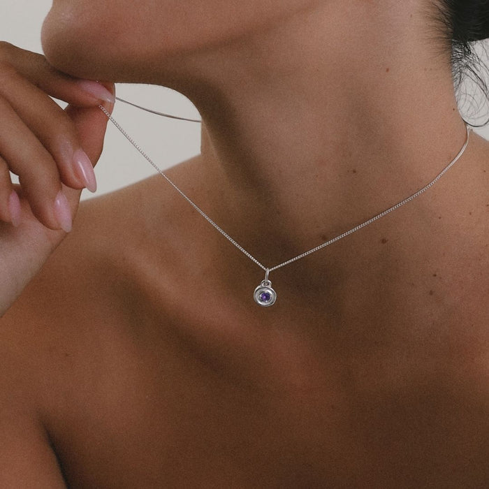 Close-up of a silver necklace with a pendant on a person's neck.