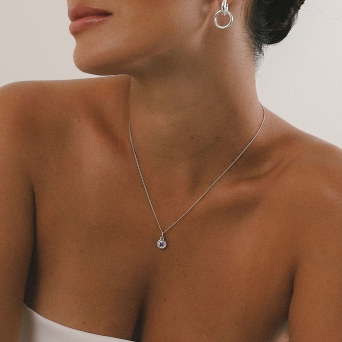 Close-up of a person wearing a silver necklace and earring on a neutral background