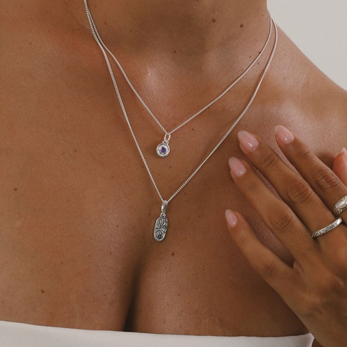 Close-up of a person wearing two silver necklaces with pendants on a neutral background