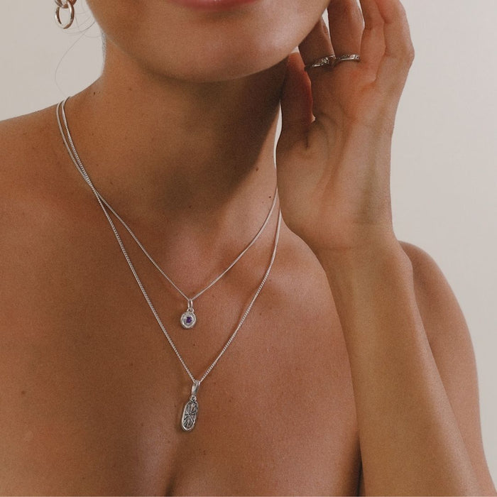 Close-up of a person wearing two silver necklaces with pendants on a neutral background