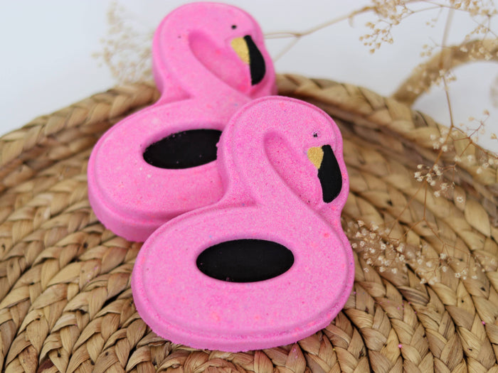 Bright pink flamingo-shaped bath bomb from Sudsy Soap Works LLC, with colorful floral accents, ready for a relaxing bath.