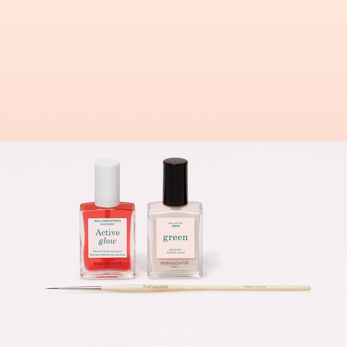 Two bottles of Manucurist French Manicure Glow polish are side by side with a thin nail art brush in front, set on a light pink background—ideal for creating a gel-like shine and the perfect French manicure.