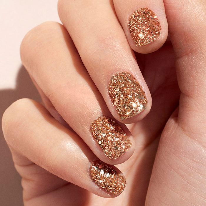 A close-up of fingernails painted with Manucurist’s Glitters Duo Rose Gold  Glazed shows a sparkling, pearlescent shine that catches the light for a festive, glamorous look.