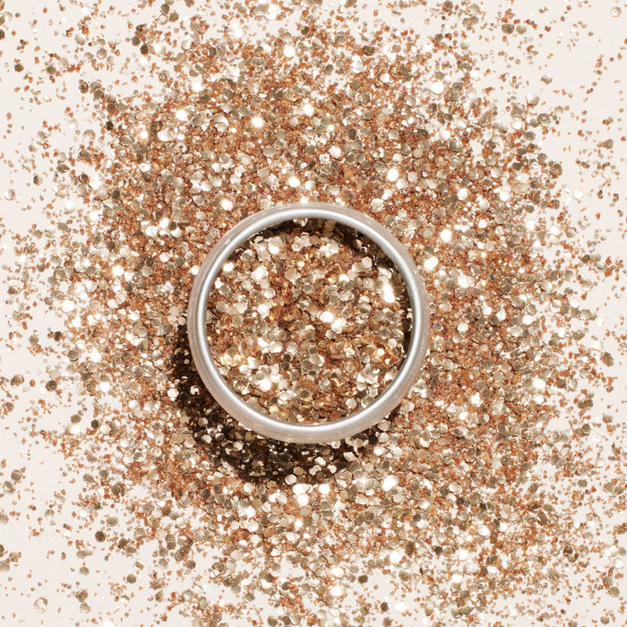 A silver ring rests on a surface dusted with Manucurist Glitters Duo Rose Gold  Glazed, creating a sparkling background with hints of rose gold and glazed shimmer.
