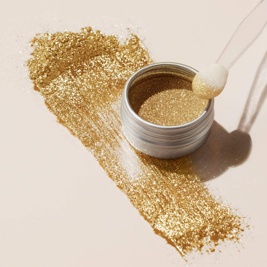 An open jar of Manucurist Golden Chrome Powder with a foam applicator sits on a light surface. Gold glitter is streaked beside the jar, revealing a shimmering chrome finish similar to Golden Chrome Powder.