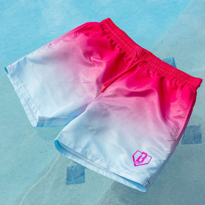BL101 pink to white ombre swim trunks with pink drawstring waistband and pink BL101 home plate logo, laid flat on a pool deck.