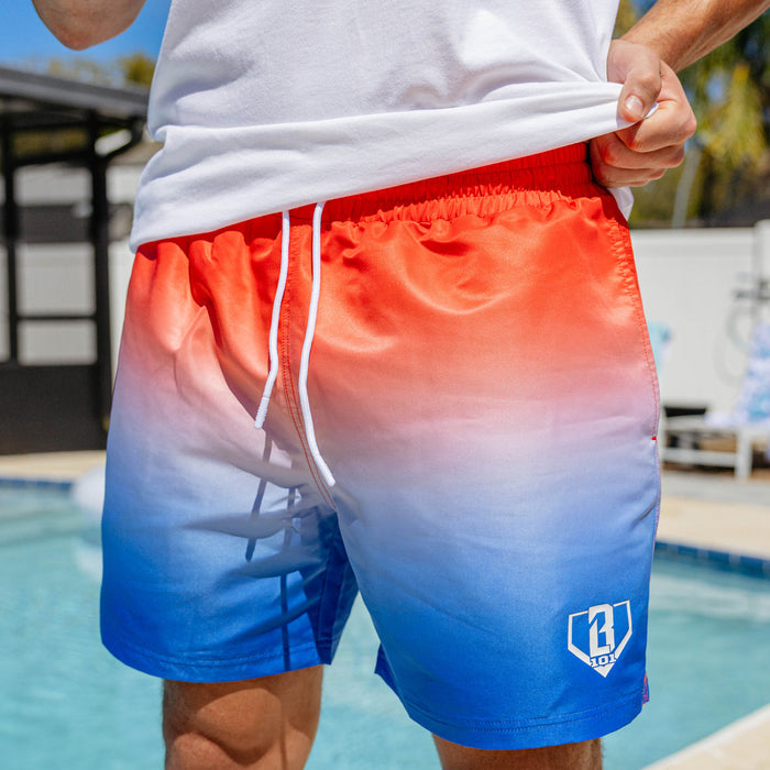 Close-up of BL101 red to blue ombre swim trunks worn poolside with a white drawstring and BL101 home plate logo on the leg.