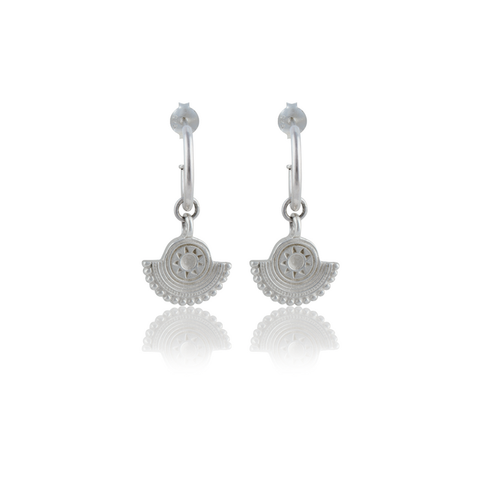 A pair of silver earrings with a circular sunburst design on a white background.